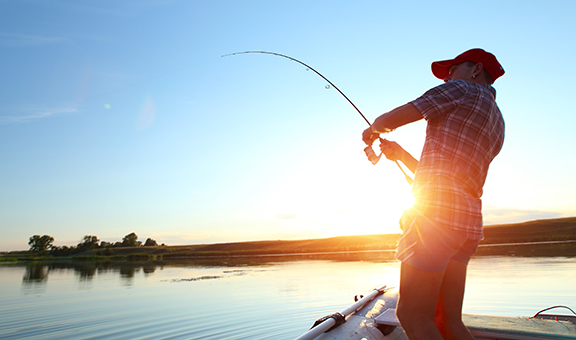 Young man fishing on a lake from the boat at sunset